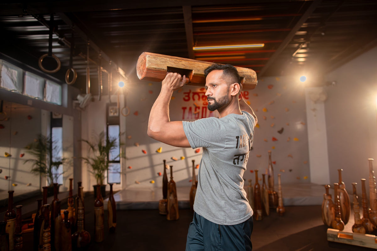 A Tagda Raho athlete carrying a raw seasoned log across the shoulders at the training ground